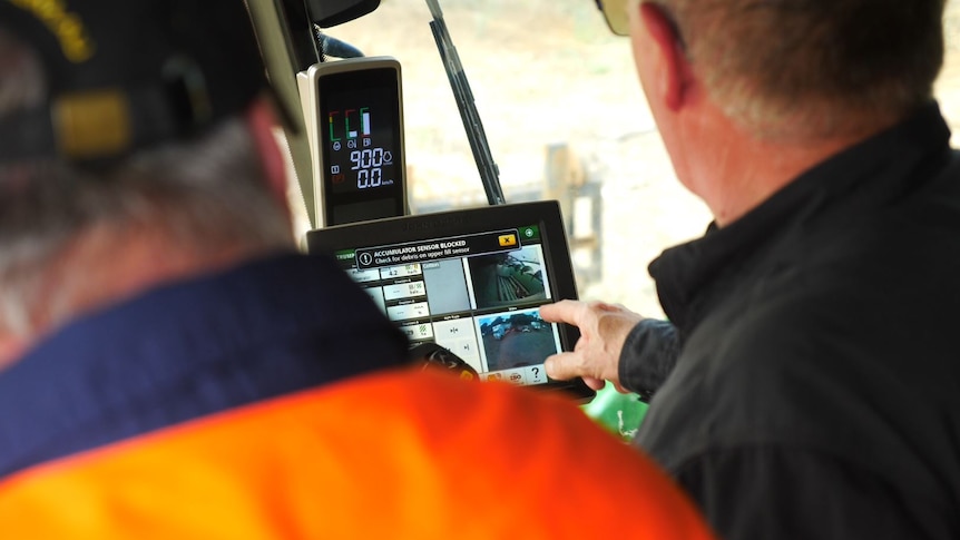 A man shows another man how to operate a touchscreen on a large item of farm machinery