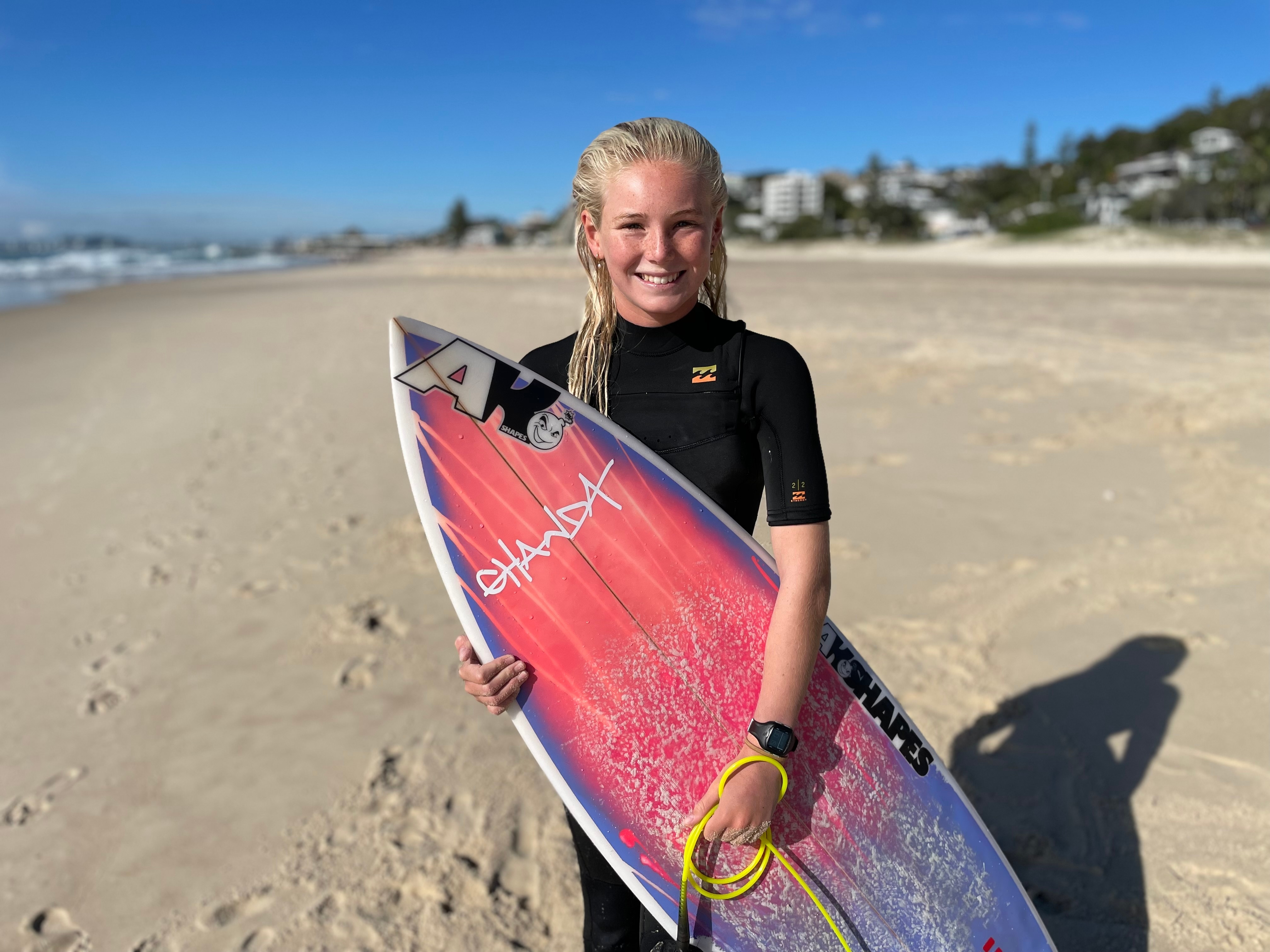 a young female surfer in a wetsuit standing on the beach with her surfboard