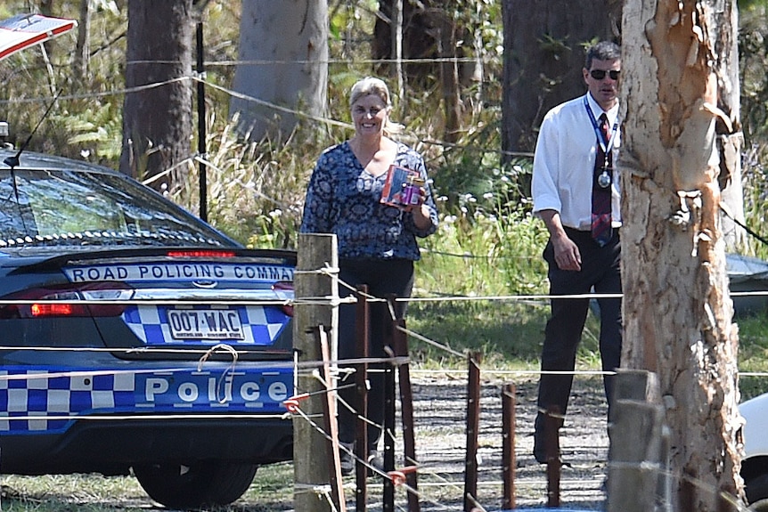 Julene Thorburn stands and smiles beside a police car at her property at Chambers Flat, south of Brisbane.