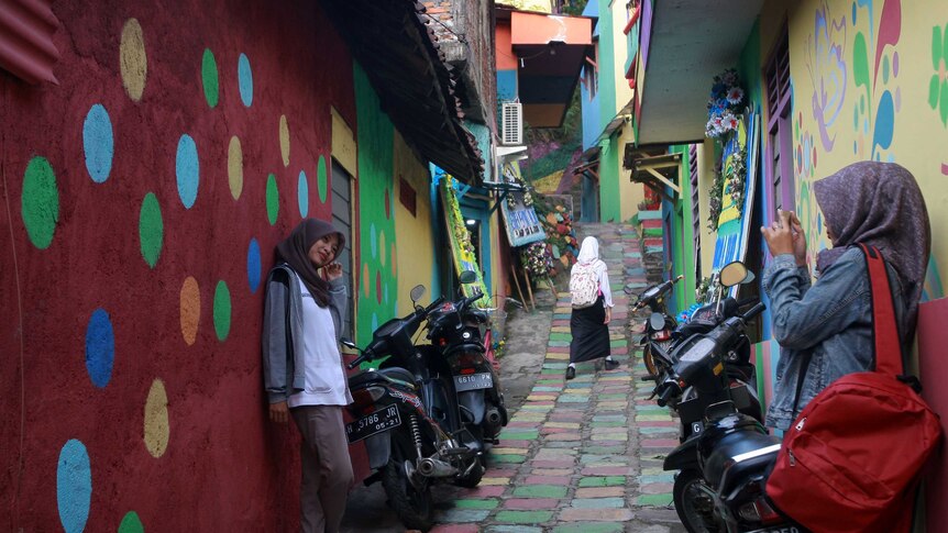 Two young women take photos in colourful alleyway in a Wonosari Village, Semarang Central Java, Indonesia.