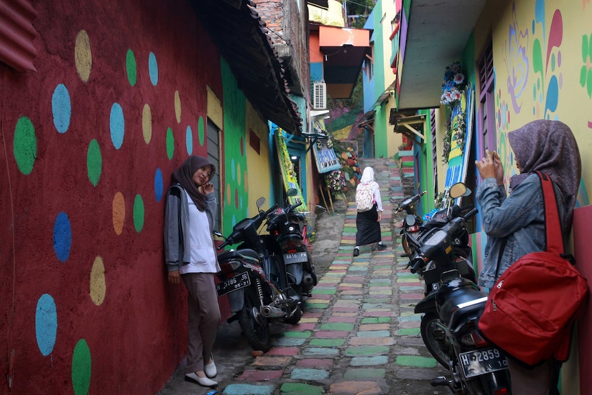 Two young women take photos in colourful alleyway in a Wonosari Village, Semarang Central Java, Indonesia.