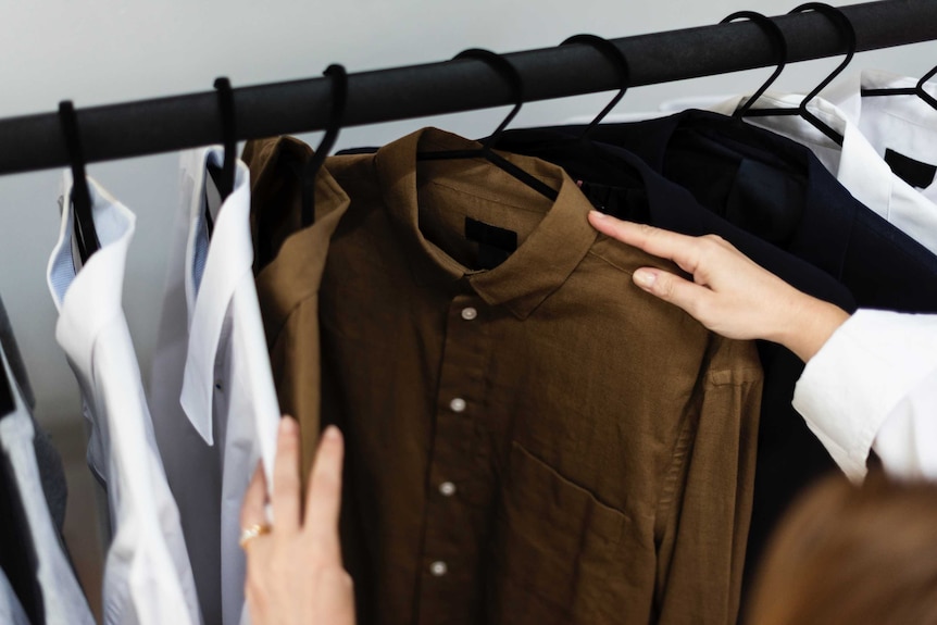 A hand flicks through shirts on a clothing rack, representing the underlying causes of irresponsible spending leading to debt.
