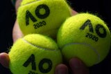 Close-up of a hand holding three Australian Open-branded tennis balls.