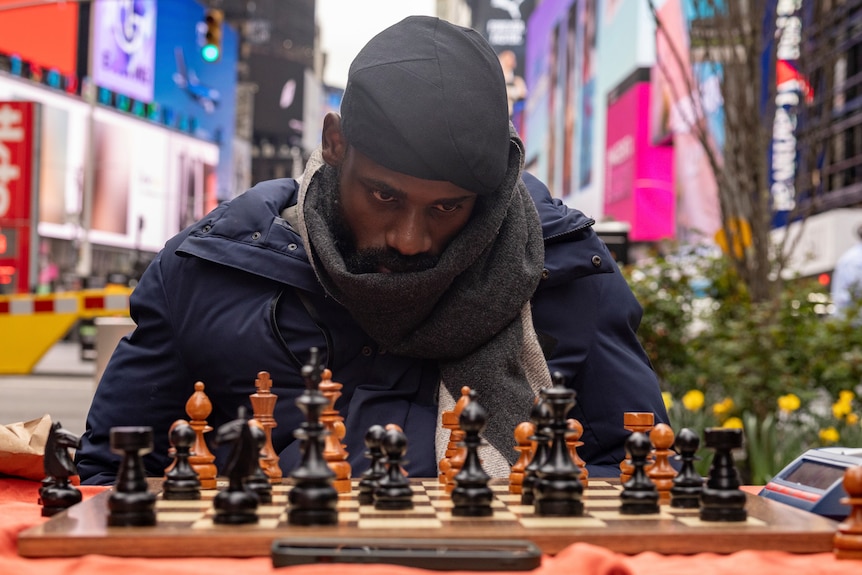 A man sitting at a chess board in times square. 