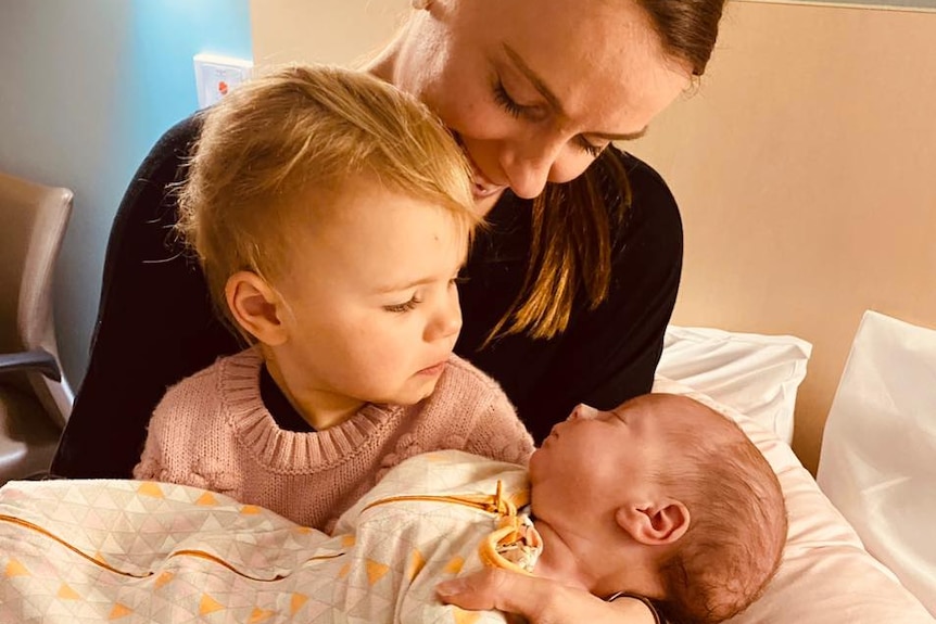 A woman sits on a bed with two children in her lap.