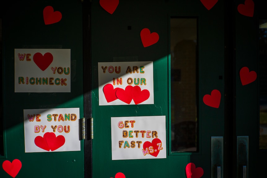 A dark green school door is plastered with messages of support for the shot teacher.