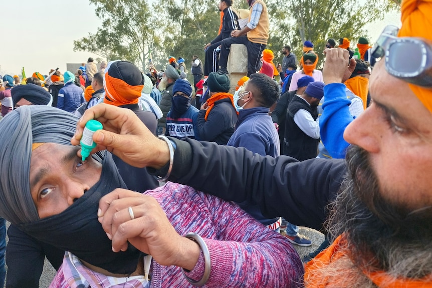 A farmer administers eye drops to a fellow protester as a precaution against tear gas.