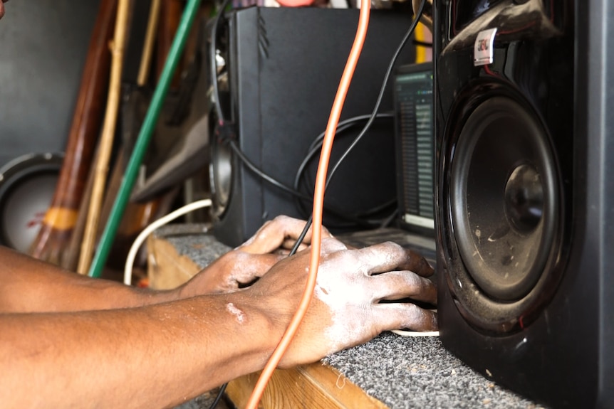 a person's hands typing on a lap top next to large dusty speakers