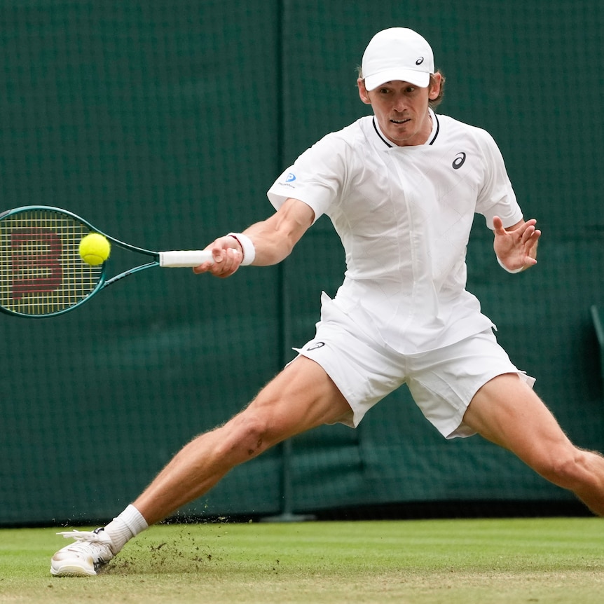 Alex de Minaur slides to hit a forehand during a tennis match at Wimbledon.