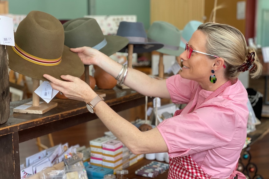 Woman in pink shirt and red glasses adjusts hat on stand 