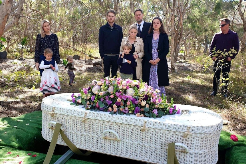 A family looking sad underneath trees at a burial site.