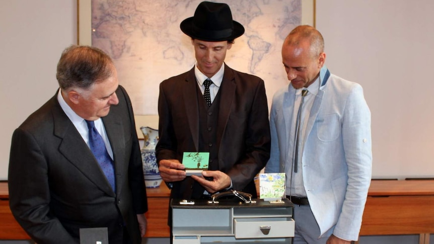 Spanish ambassador Enrique Viguera, artist Peter Burke and Cesar Espada, deputy head of mission opening the briefcase that's part of the Low Cost Diplomatic Bag Project.