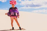 A man in brightly coloured drag costume standing on a sand dune