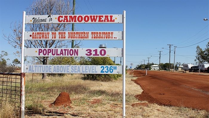 A white sign on the side of the road welcoming travellers to the town of Camooweal.