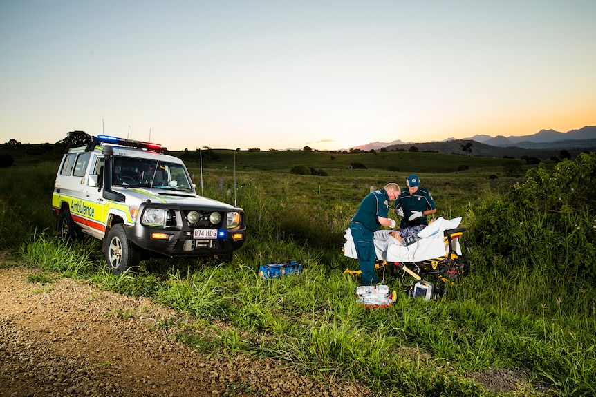 Ambulance officers treating a patient on the side of a country road.
