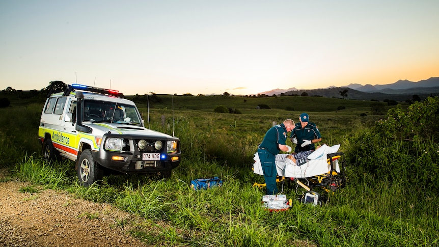 Two paramedics treat a patient in a bed at the side of the road.
