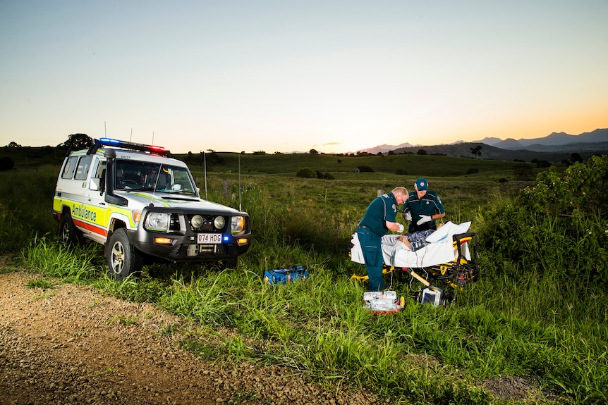 Two paramedics treat a patient in a bed at the side of the road.