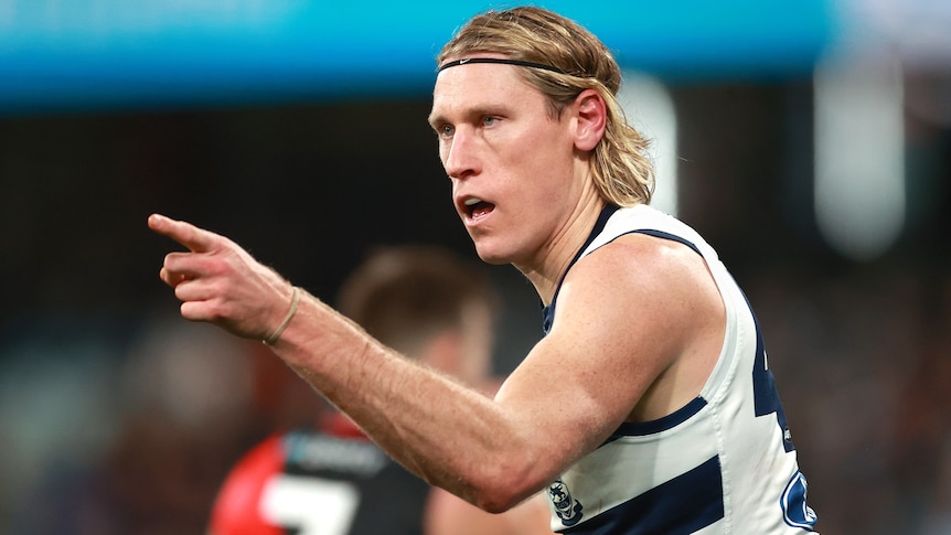 A Geelong AFL player points a finger on his left hand as he celebrates a goal against Essendon.