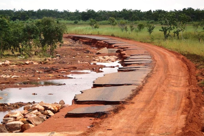 a heavily flood-damaged road with strips of bitumen torn away