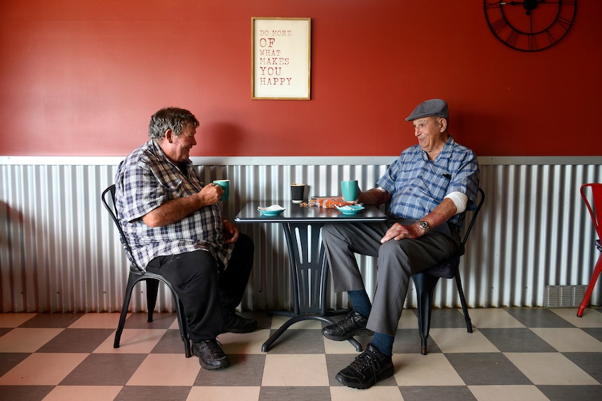 Two older men with coffee mugs sit in a cafe. 
