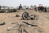 The wreckage of a motorbike and a car lay amid ruins as people mill around the aftermath of an air strike.