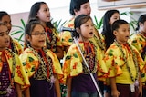 group of children singing in a choir, wearing yellow floral cloaks