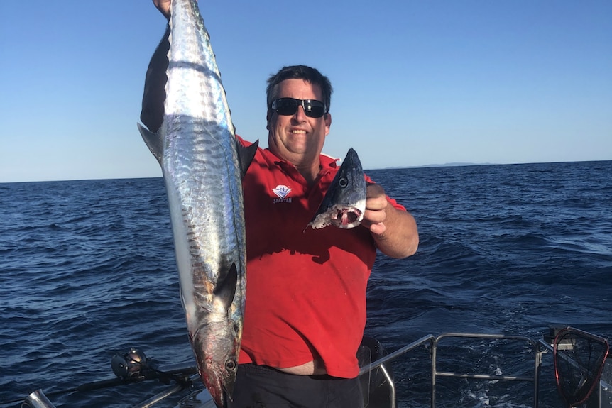 Holding up a big fish in one hand, and the head of a fish that has been bitten off, in the other hand.