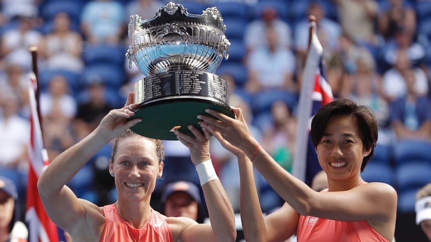 Two tennis players hold the trophy after winning the Australian Open women's doubles final.