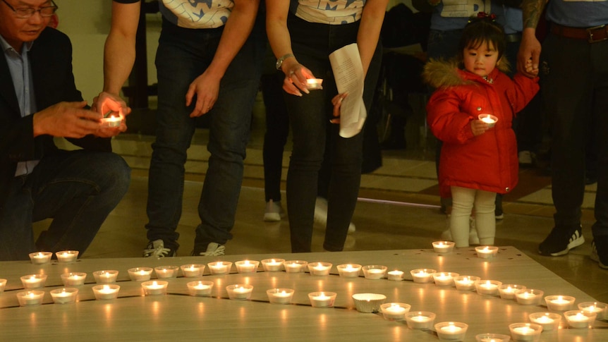 People place candles, a small girl in a red jacket holds a candle