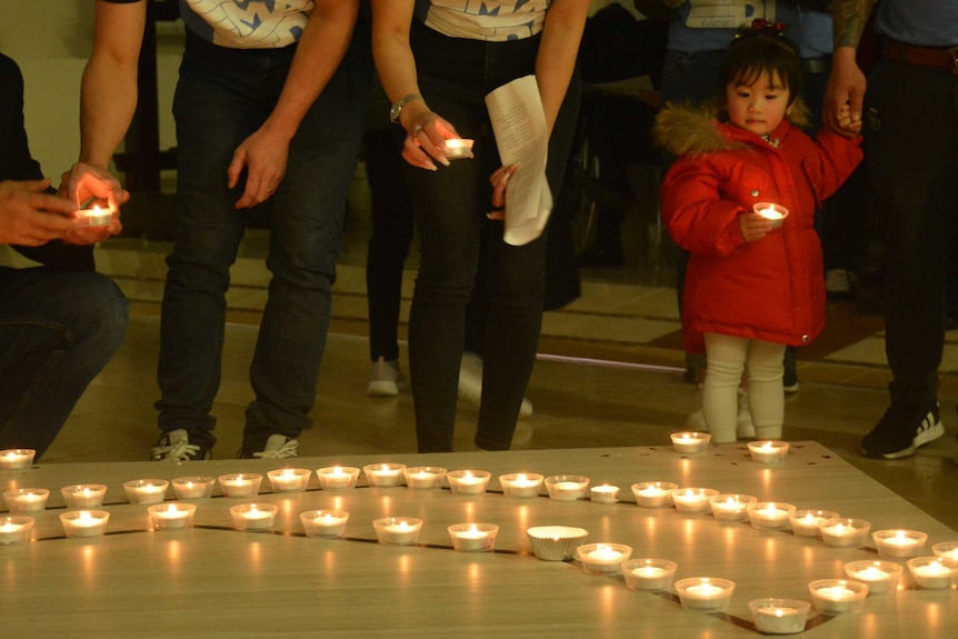 People place candles, a small girl in a red jacket holds a candle