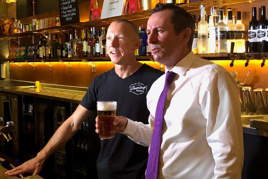 Mark McGowan holds a beer while standing behind The Sewing Room bar with owner Martin Black.