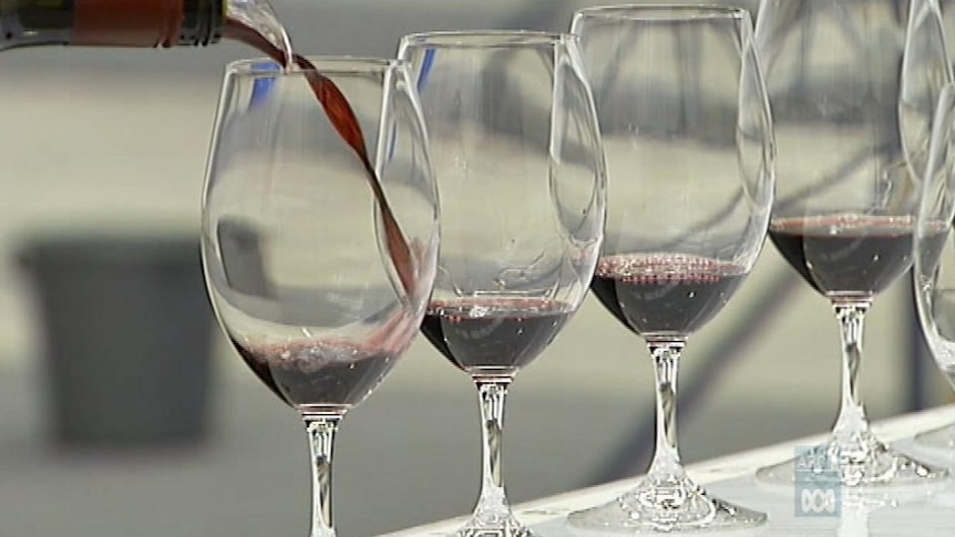 Wine is poured into a glass on a white bench, with several other glasses placed next to it.