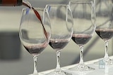 Wine is poured into a glass on a white bench, with several other glasses placed next to it.