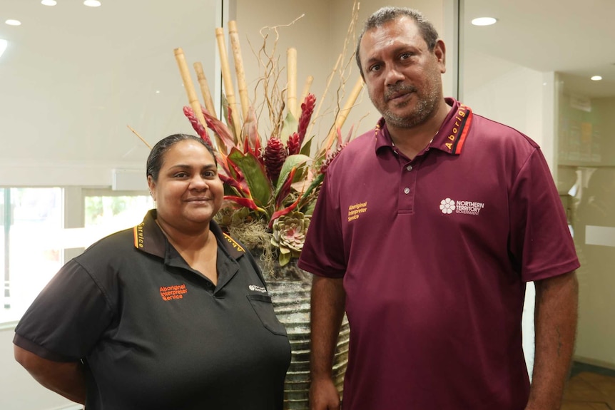 Male and female AIS spokespeople smiling at camera with flowers in the background.