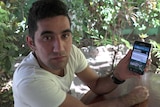 Manus Island detainee Benham Moghimi holding his phone with an ABC News story about $70 million compensation on it