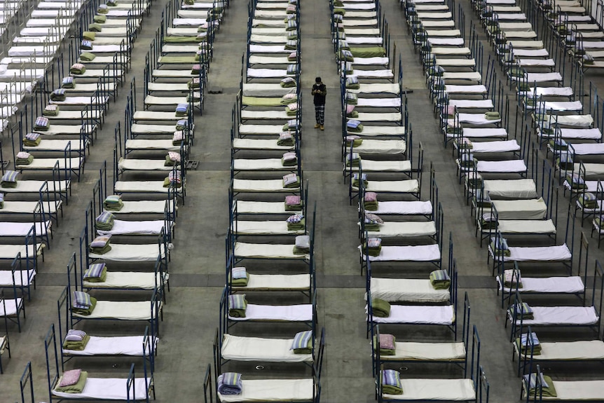 A man stands in the middle of rows of beds in a large convention centre.