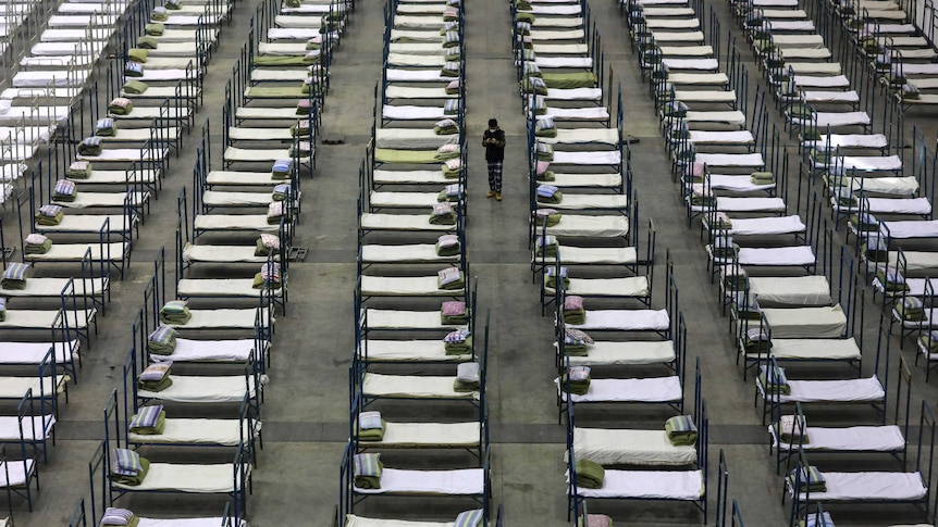 A man stands in the middle of rows of beds in a large convention centre.