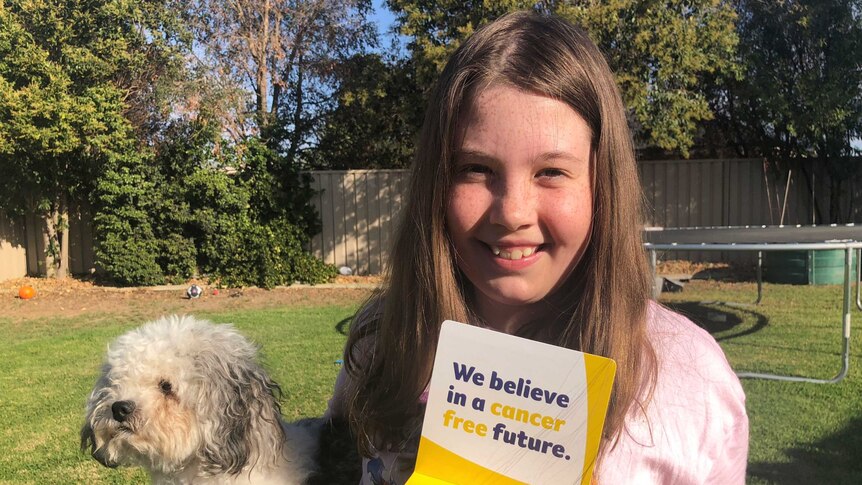 10-year-old Claire Anschuetz standing in her backyard with her fundraising box and her dog
