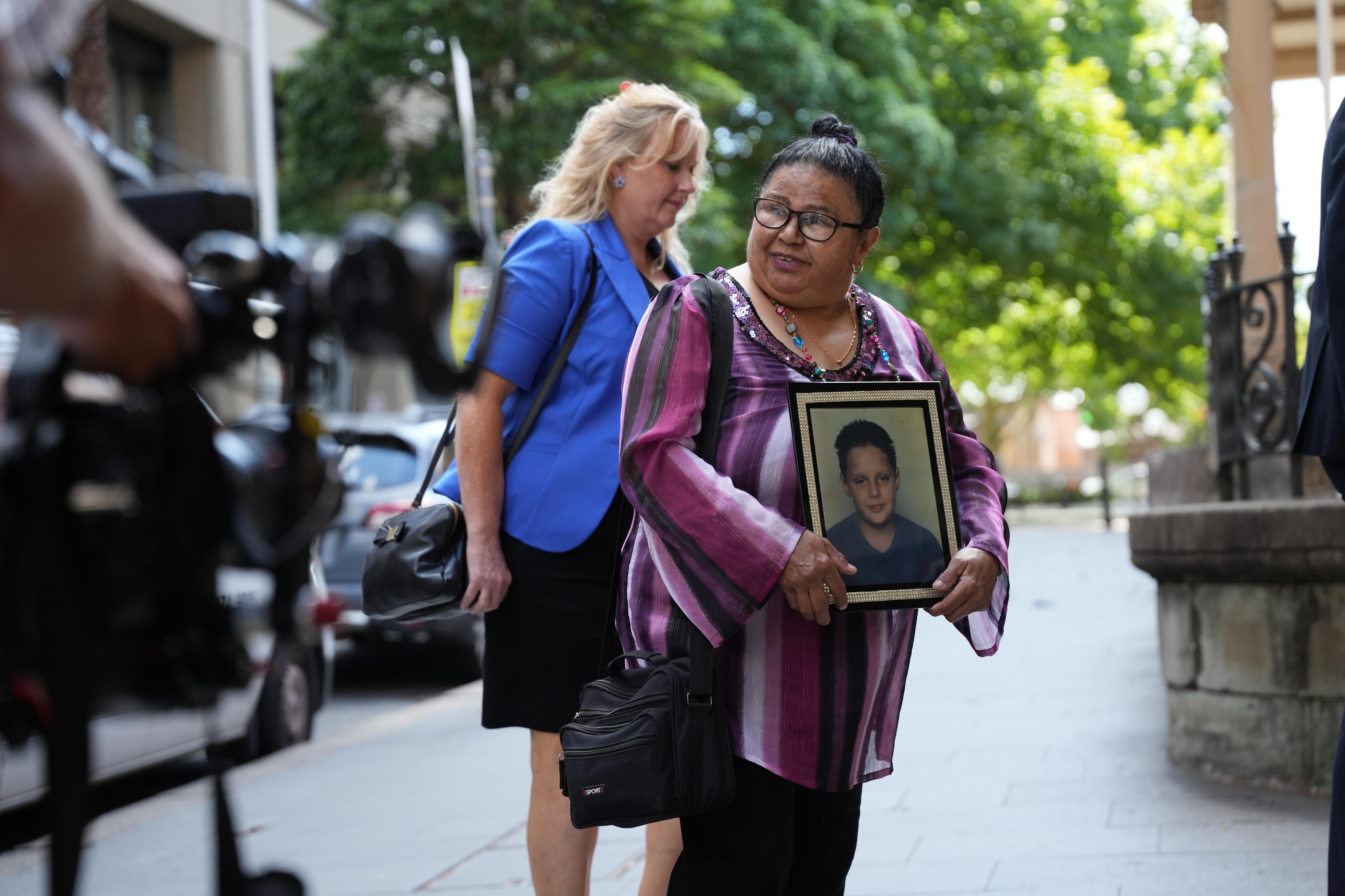 Uma mulher sorri do lado de fora do tribunal e segura a foto de uma criança