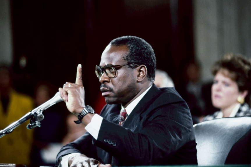 An old photograph of Clarence Thomas with his hand in the air