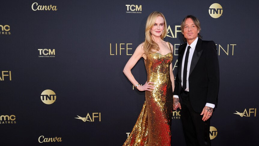 Nicole Kidman wearing a long strapless gold sequin dress with a long strain with Kieth Urban in a black suit