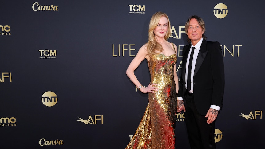 Nicole Kidman wearing a long strapless gold sequin dress with a long strain with Kieth Urban in a black suit