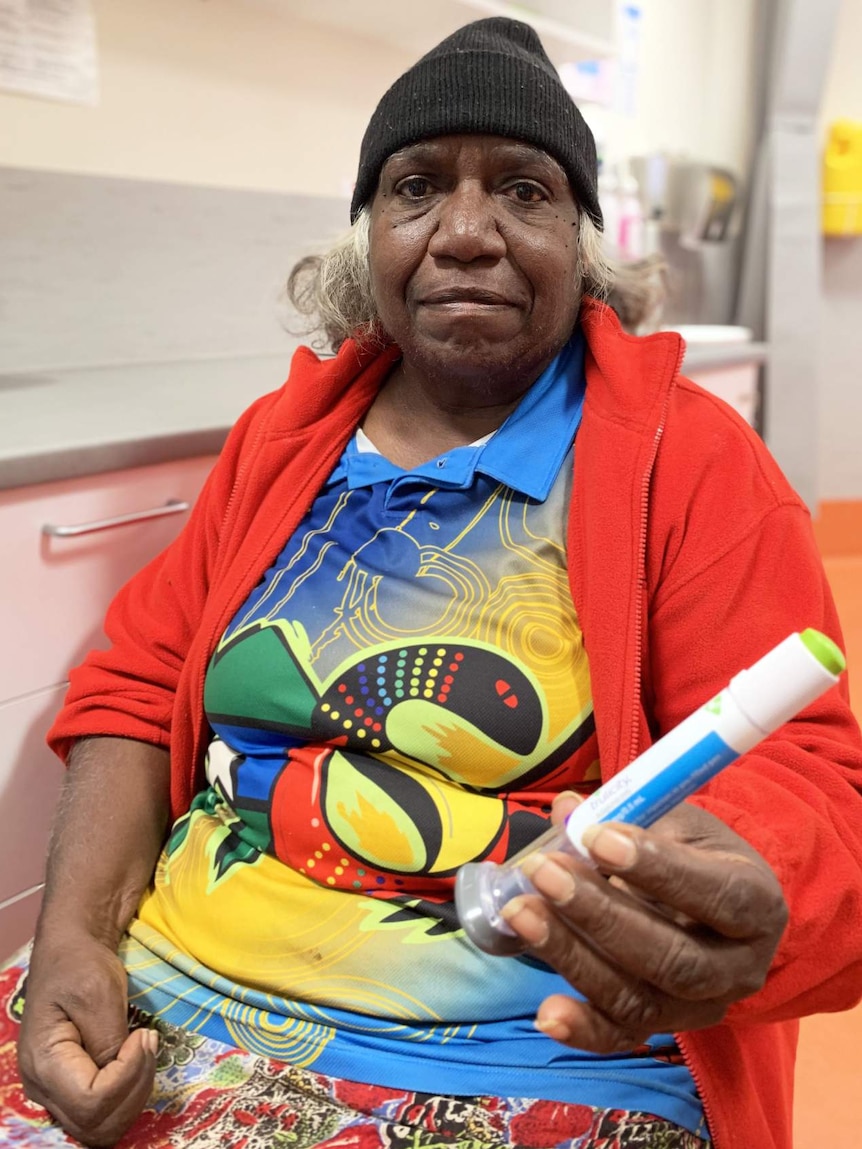 A woman sitting in a chair holds a capsule containing an injection for diabetes.