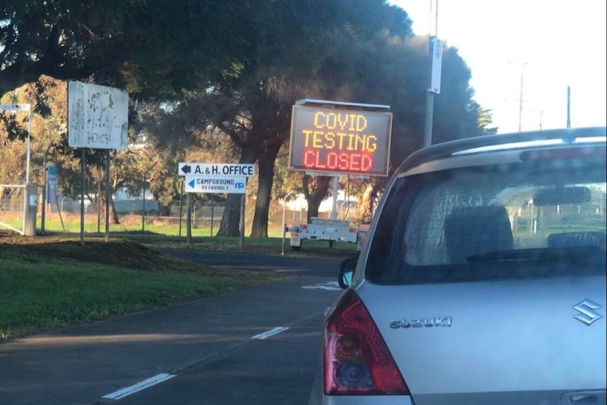 An electronic sign reading 'COVID testing closed' with a car in front