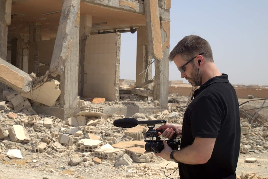 A man films the crumbling remains of a building in the desert.