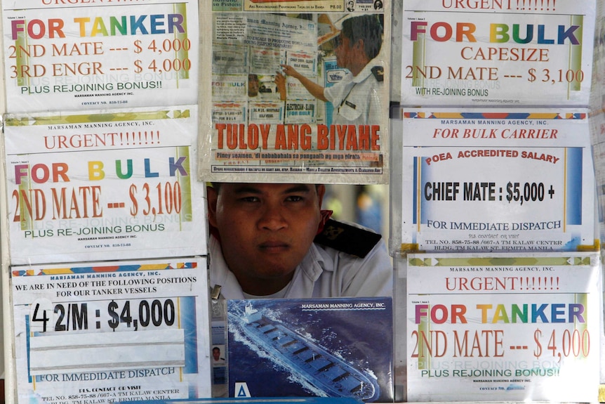 You view a man sitting behind a wall of flyers advertising shipping jobs in an outdoor booth in Manila.