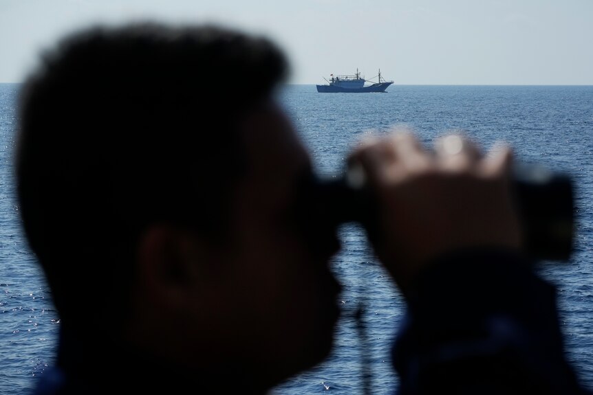 Sillouette of man wearing binoculars in front of sea 