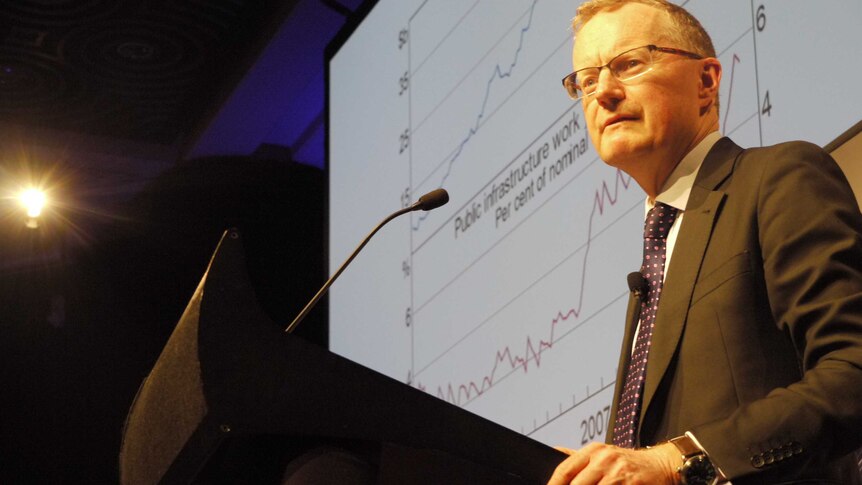 Reserve Bank Governor Philip Lowe stands at a dais speaking in front of a screen showing a graph.