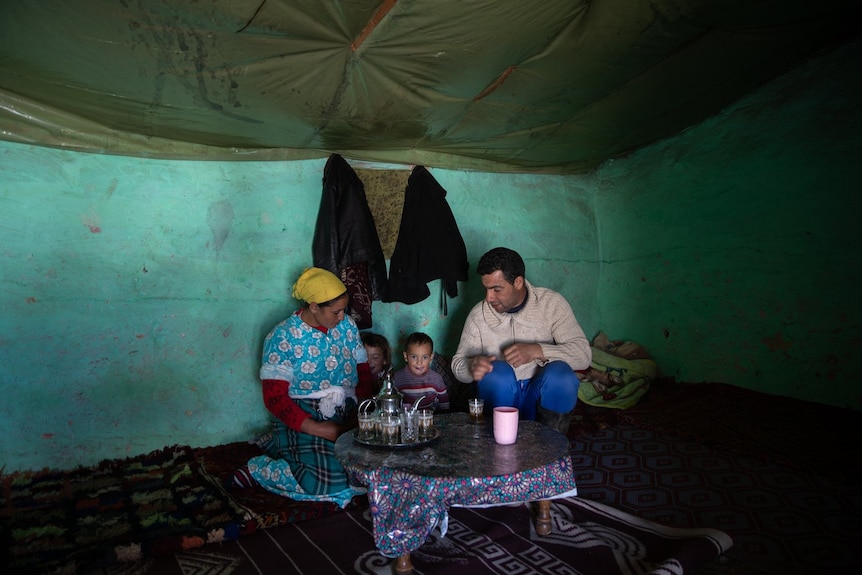 A family of four sits and has tea against a teal wall.