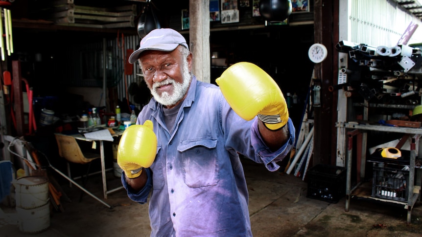 Older man holding up yellow boxing gloves.